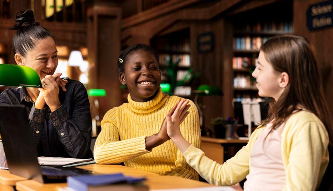 High school students sitting in a library and giving each other a high five working on schoolwork